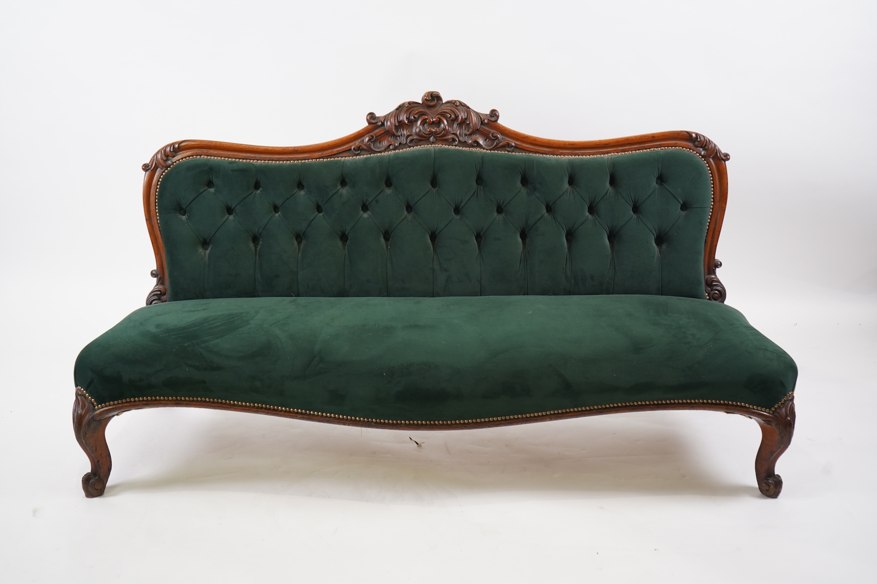 A pair of Victorian carved oak settees, recently re-upholstered in deep buttoned green velvet, the scroll carved crest rails over serpentine seats on cabriole front legs, 160cm wide, 96cm high, Provenance - previously gi